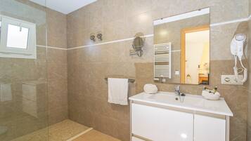 Un baño moderno con cabina de ducha de vidrio, un lavabo blanco con dos cubetas, un espejo y un secador de pelo montado en la pared.