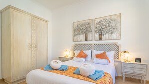 A hotel room with a large wardrobe, a bed with white linens, two bedside tables with lamps, and two wall-mounted paintings. - JUNIPER (INCA) - Cozy town house with above ground pool in the center of Mallorca. Free WI (Inca)