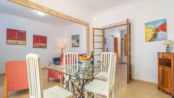 Ein Essbereich mit einem Glastisch, weißen Stühlen und einem roten Sofa. An den Wänden befinden sich Gemälde und es gibt einen Holzschrank.