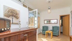 A modern living room with a wooden cabinet, a green sofa, a small table, and a large window. - JUNIPER (INCA) - Cozy town house with above ground pool in the center of Mallorca. Free WI (Inca)