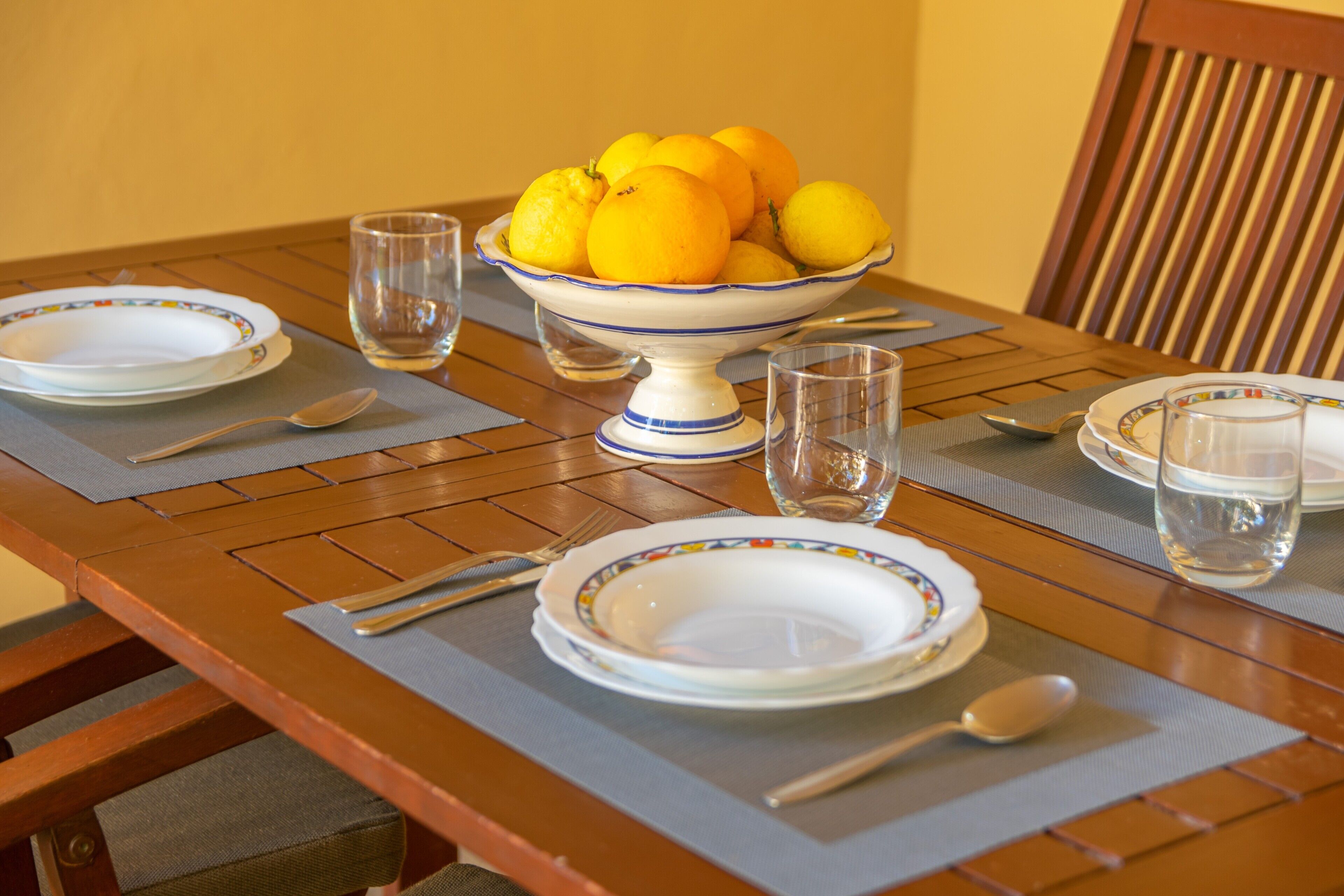Una mesa de comedor dispuesta con platos, cubiertos y un bol de limones.