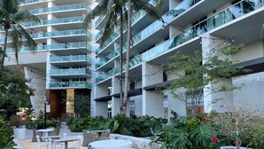Un hôtel moderne doté d’une cour intérieure avec des espaces de détente en plein air, des palmiers et un immeuble à plusieurs étages avec des balcons.