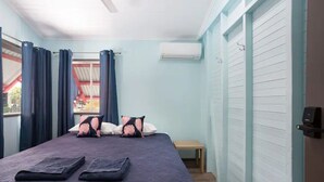 Ein Schlafzimmer mit Bett, Kissen, einer Bank, einer Klimaanlage und einem Fenster mit Vorhängen.