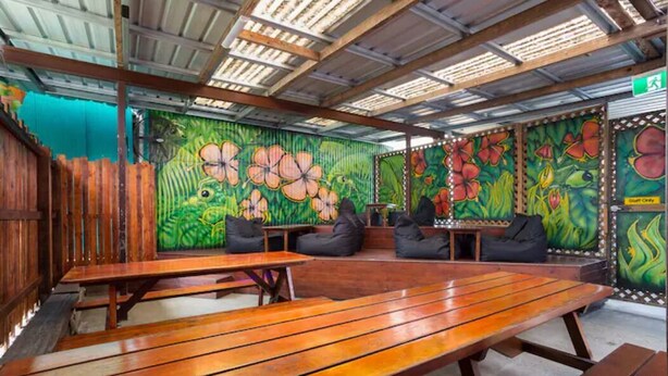 Ein Innenraum mit Holzbänken und -tischen, lebhaften floralen Wandmalereien und einer Metall-Deckenkonstruktion.