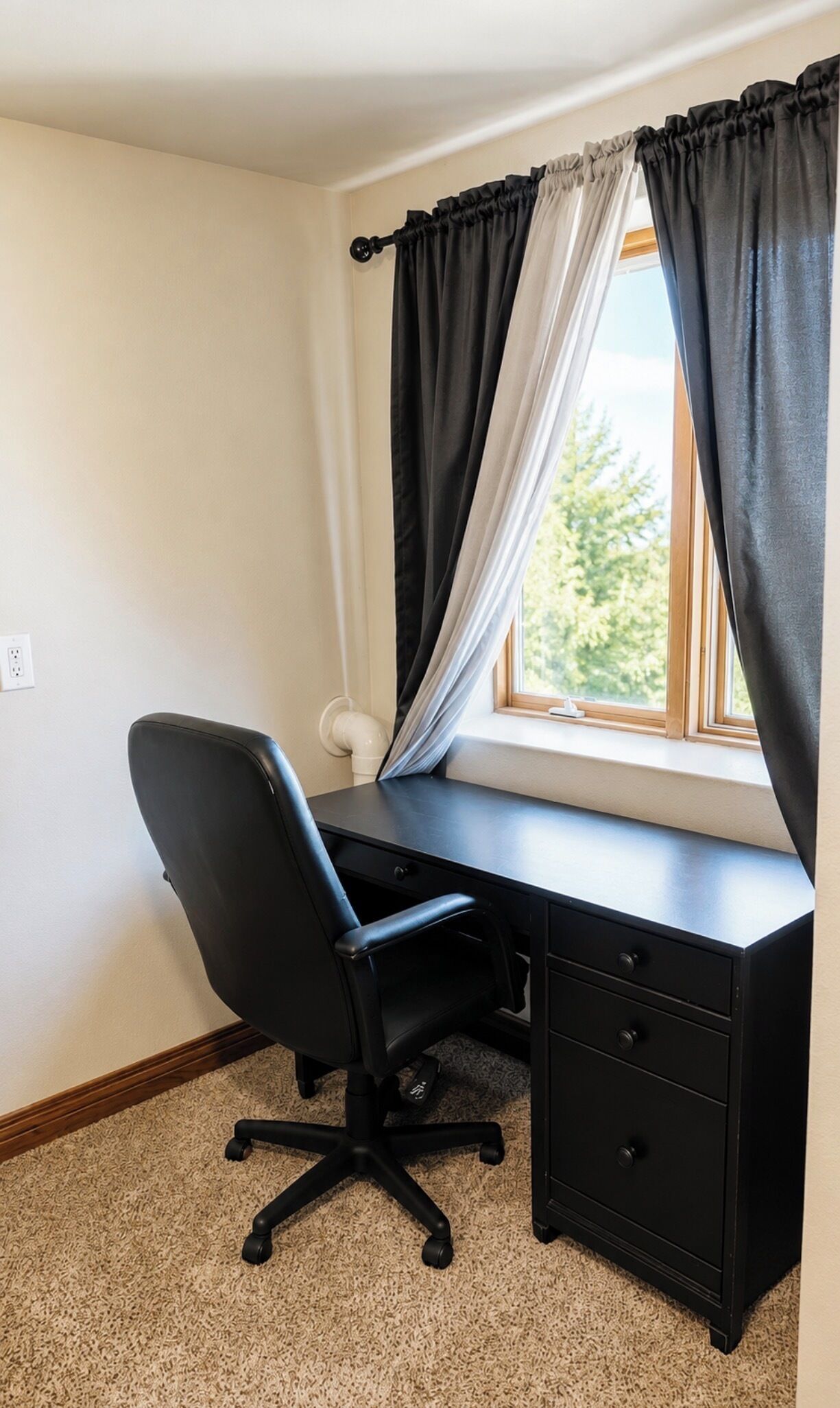 A corner office with a desk, chair, and window with curtains.