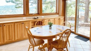 A kitchen with wooden cabinets, a round dining table with chairs, and large windows with a view of trees and mountains. - Mountain Retreat Near Red Rocks -Private Deck -Mountain Views - Hike, Bike, Ski (Golden)