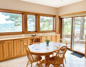 Una cocina con armarios de madera, una mesa redonda con sillas y amplias ventanas con vistas a árboles y montañas.