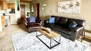 A living room with a brown leather sofa, a wooden coffee table, and a patterned rug. - Mountain Retreat Near Red Rocks -Private Deck -Mountain Views - Hike, Bike, Ski (Golden)