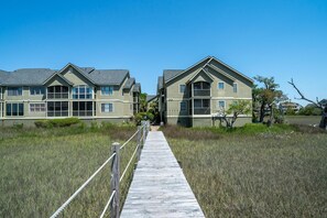 A pathway leading to a row of two-story buildings with large windows and balconies, surrounded by grassy areas.