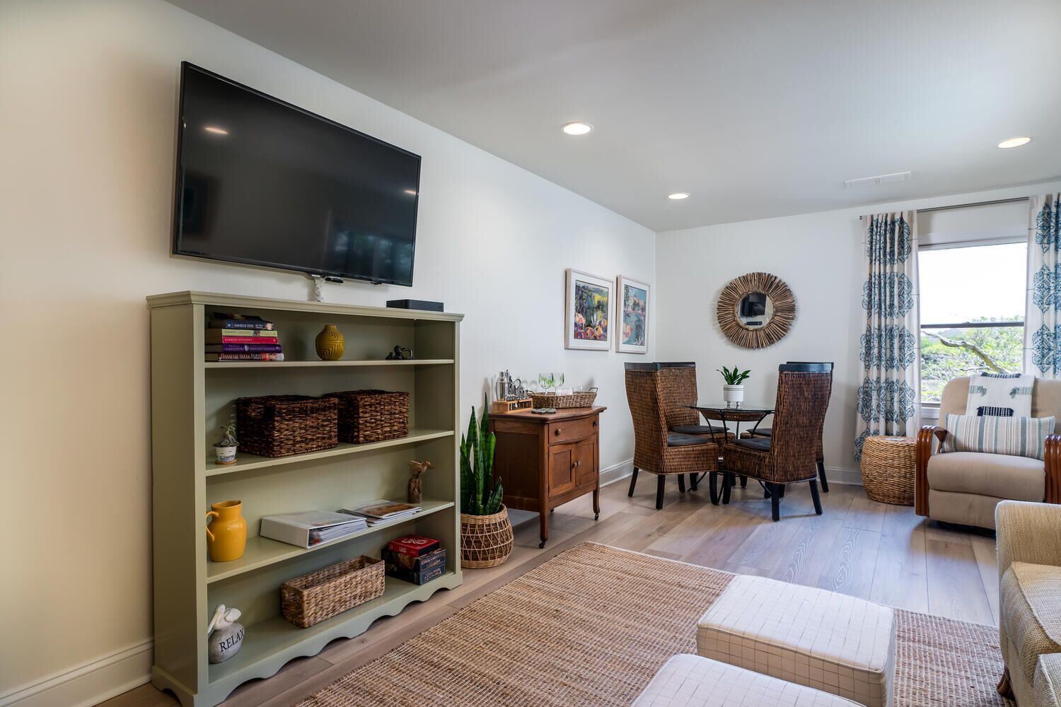 A living room with a flat-screen TV, wicker furniture, and a dining area with chairs and a table.