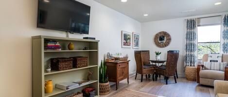 A living room with a flat-screen TV, wicker furniture, and a dining area with chairs and a table.