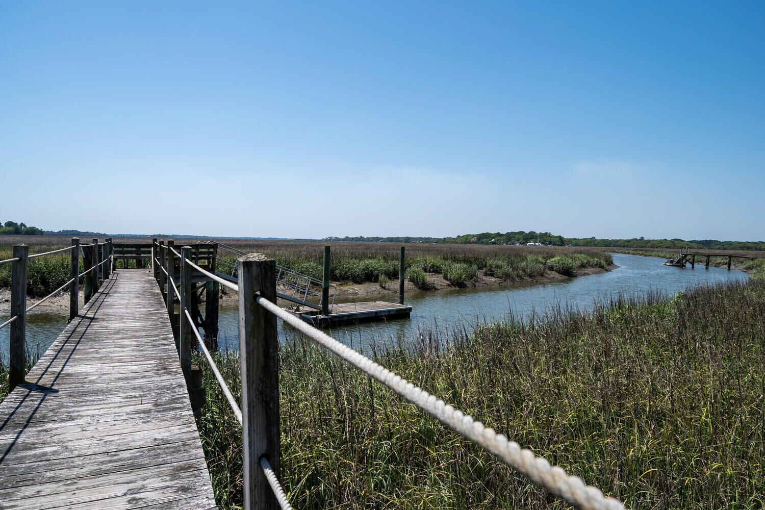 A wooden boardwalk leading to a riverbank with a small dock.
