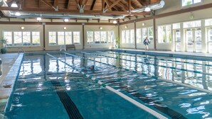 Una piscina interior con agua cristalina, vigas de madera en el techo y ventanas amplias.