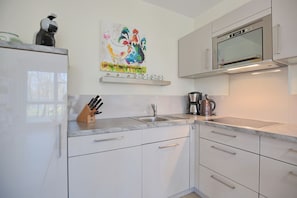 A modern kitchen with white cabinets, a stainless steel sink, a coffee maker, and a microwave. - Strandglück Apartment 4A**** - Strandglück House A (Scharbeutz)