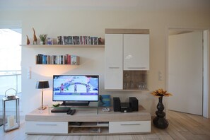 A living room with a TV displaying a sports event, a bookshelf, a cabinet, and a vase with flowers.