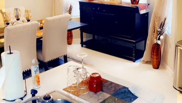 A modern kitchen with a double sink, a dining area with a table and chairs, and a dark-colored cabinet in the background. - Relax near downtown Atlanta (Lithonia)