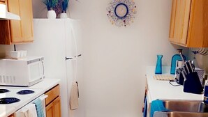 A compact kitchen with wooden cabinets, a white refrigerator, a microwave, a stove, and a sink. There are two rugs on the floor and a decorative wall piece above the sink. - Relax near downtown Atlanta (Lithonia)