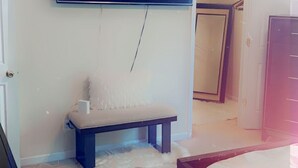 A bedroom with a large flat-screen TV mounted on the wall, a bench with a fluffy cushion, a patterned rug, and a bed with a wooden frame. - Relax near downtown Atlanta (Lithonia)