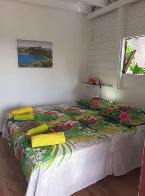 A bed with a floral bedspread, a painting of a coastal landscape, and a window with blinds. - Villa le chalet des iles in the countryside with private pool (ST FRANCOIS)