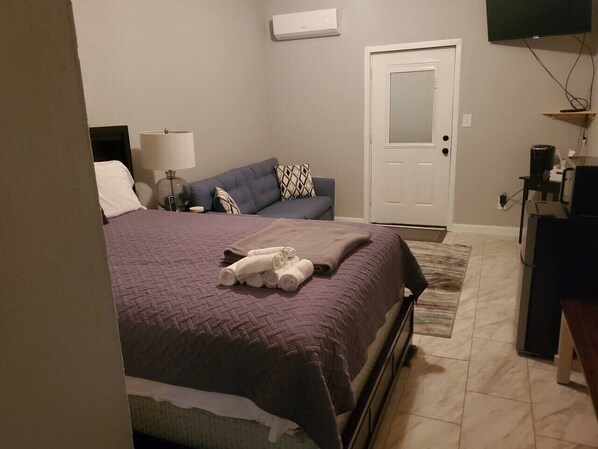 A bedroom with a bed, a sofa, a TV, and a coffee machine.