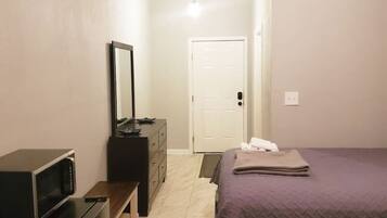 A bedroom with a bed, a dresser, a microwave, and a door.
