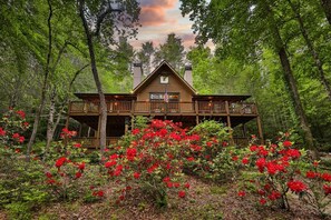 Une cabane dotée d’un balcon, entourée d’arbres et de fleurs rouges.