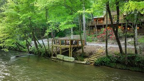 Een houten terras met stoelen met uitzicht op een rivier, omgeven door dicht bos.