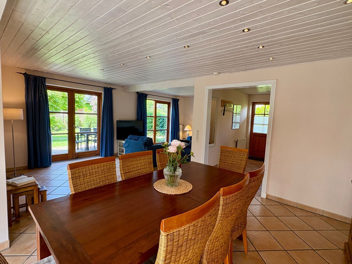 A dining area with a wooden table, wicker chairs, and a vase with flowers.
