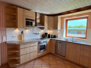 A compact kitchen with wooden cabinets, a microwave, stove, and dishwasher. - Theodor Heuss - Theodor-Heuss Vacation Home, 15, 130 m² for up to 8 people (Sylt)