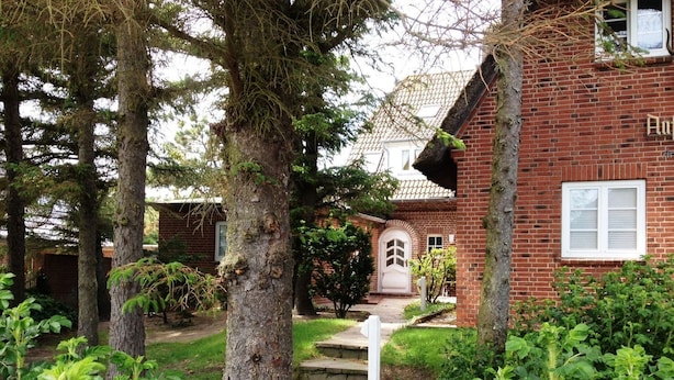 Un edificio in mattoni con una porta bianca e un piccolo giardino con alberi e piante.