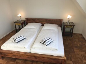 Een tweepersoonsbed met witte lakens en gestreepte handdoeken, twee nachtkastjes met lampen, en een houten hoofdbord.