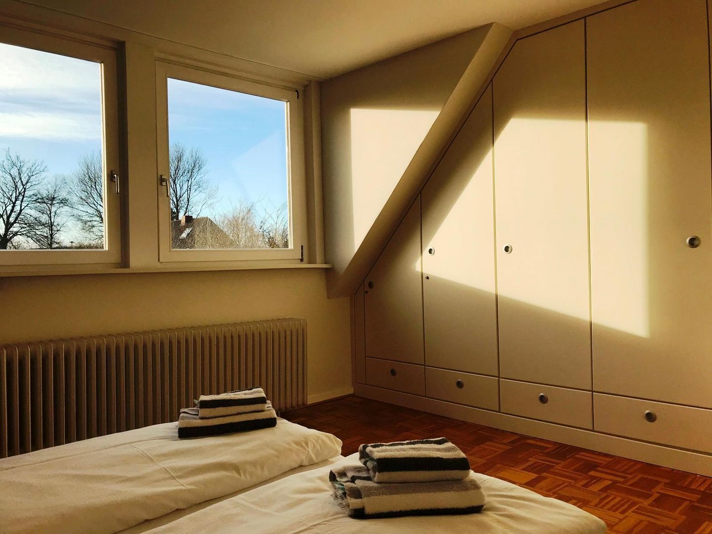 A bedroom with two beds, a window, a radiator, and a wardrobe.