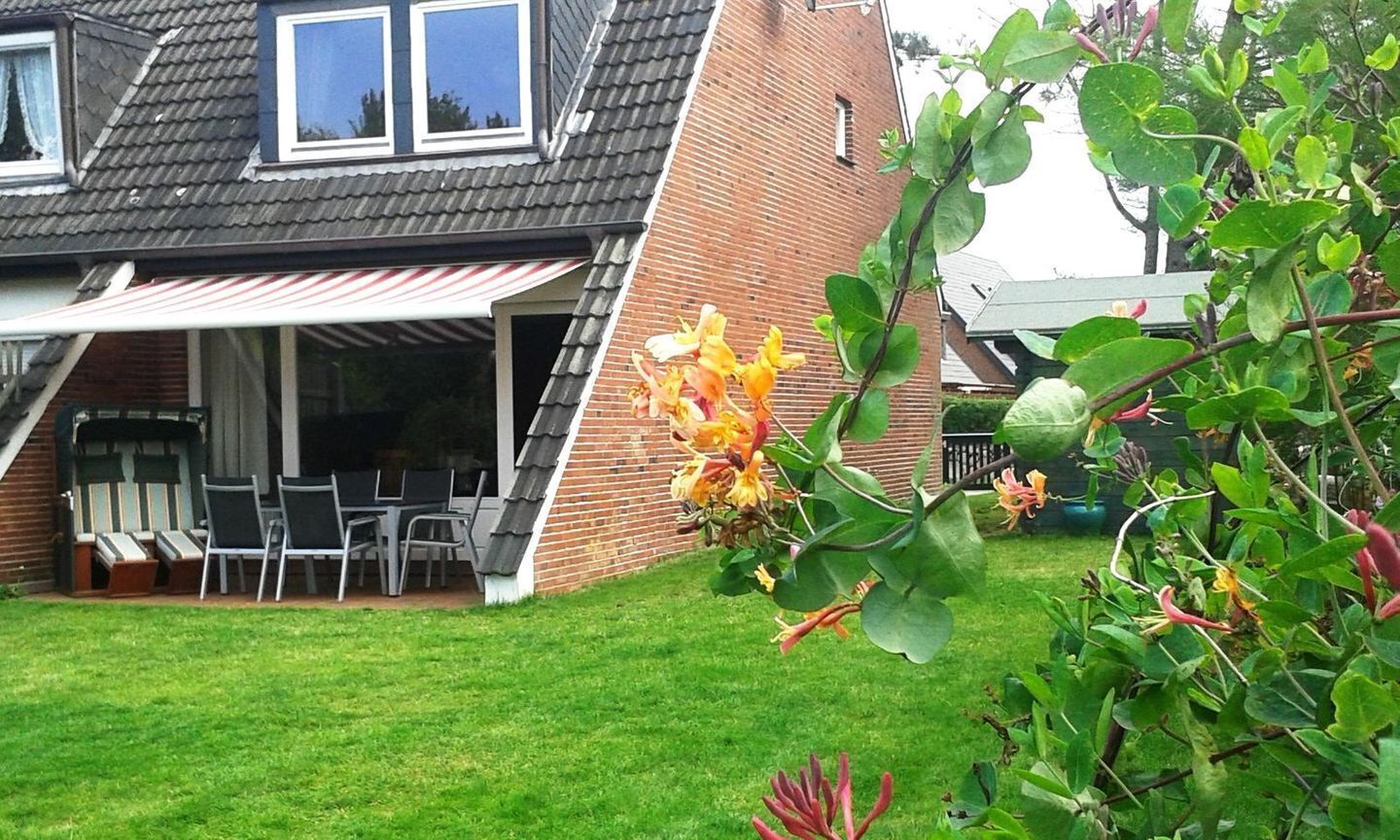 A residential backyard with a covered patio, a brick house, and a garden with flowering plants.