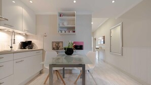 A modern kitchen with white cabinets, a glass dining table, and a coffee maker. - 2nd Seahorse, 70sqm for up to 2-3 persons - Villa Frische Brise (Sylt)