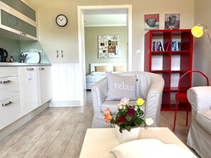 Un soggiorno moderno con un divano grigio, una libreria rossa e un angolo cottura con mobili bianchi.