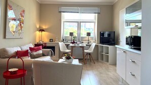Una sala de estar moderna con sofá, mesa de comedor y zona de cocina, con televisor y microondas.