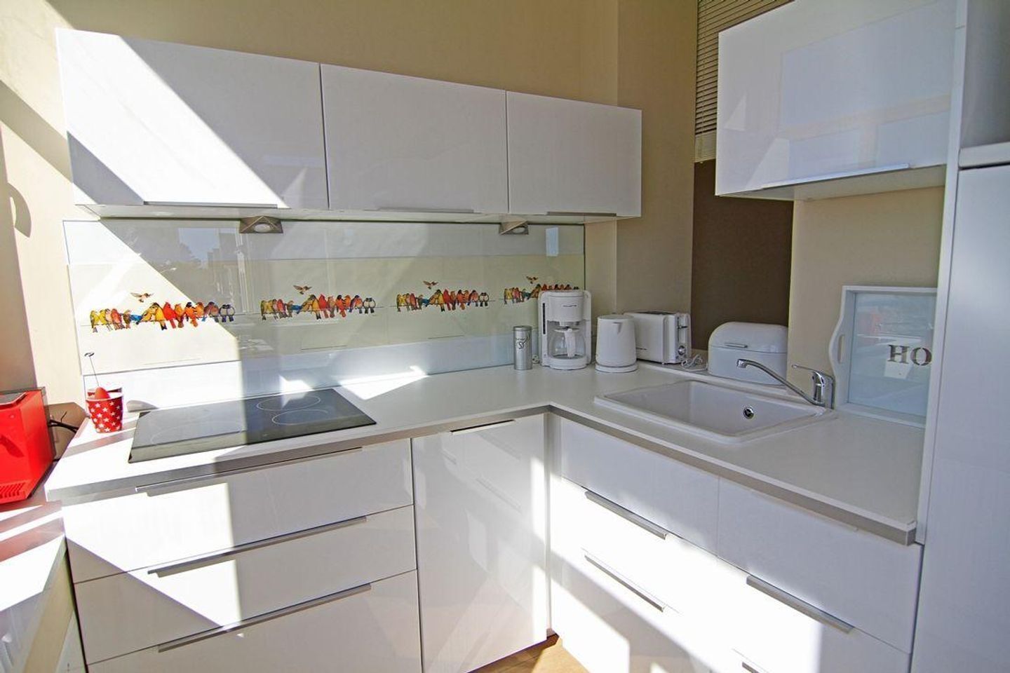 Une cuisine moderne avec des meubles blancs, un four encastré, une machine à café et un évier.
