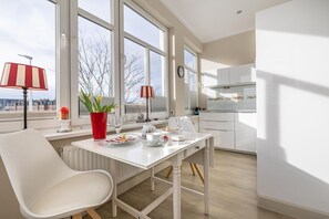 Eine moderne Küche mit weißen Schränken, einem Esstisch mit Stühlen und Blick auf die Stadt durch große Fenster.