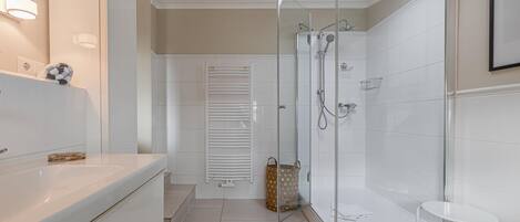 A modern bathroom with a glass shower enclosure, a white vanity with a mirror, and a small white table.