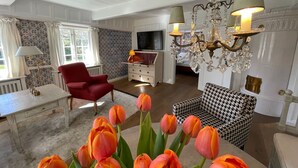 A living room with a red armchair, a houndstooth sofa, a chandelier, and tulips on a table.