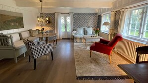 A spacious living room with a wooden floor, a dining table, a red armchair, a sofa, and a patterned wall.