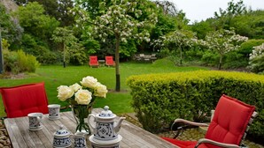 A wooden table with a tea set and red chairs in a garden setting. - 2. Studio apartment, 65 square meters, 2 bedrooms, sleeps up to 4 people - Weidemannhaus (Sylt-Ost)