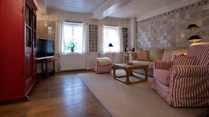 A living room with a television, striped armchairs, a wooden coffee table, and a red cabinet. - 2. Studio apartment, 65 square meters, 2 bedrooms, sleeps up to 4 people - Weidemannhaus (Sylt-Ost)