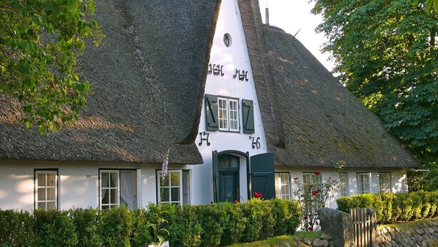 A thatched-roof house with a unique sloped roof design, a white facade, and a small window with shutters. - 2. Studio apartment, 65 square meters, 2 bedrooms, sleeps up to 4 people - Weidemannhaus (Sylt-Ost)