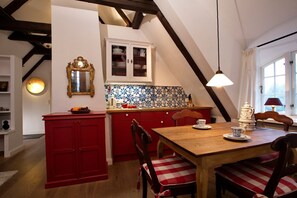Een gezellige keuken met rode kastjes, een houten eettafel en een betegelde achterwand.