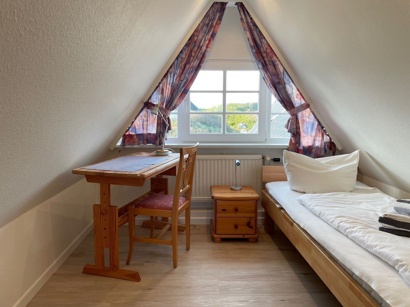 A small, triangular attic room with a wooden desk, chair, and a bed.
