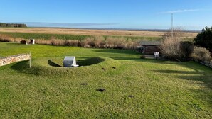 A grassy outdoor area with a stone wall, a covered grill, and a wooden structure. - Watt'n Blick, 70sqm for up to 4 people - Haus am Wattenmeer (Sylt)