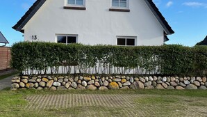 A white two-story house with a gabled roof, numbered 13, surrounded by a hedge and a stone wall. - Watt'n Blick, 70sqm for up to 4 people - Haus am Wattenmeer (Sylt)