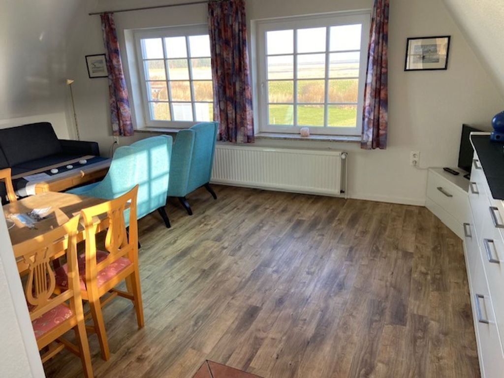 A room with a wooden floor, a dining table with chairs, a blue chair, a sofa, a radiator, and a window with curtains.