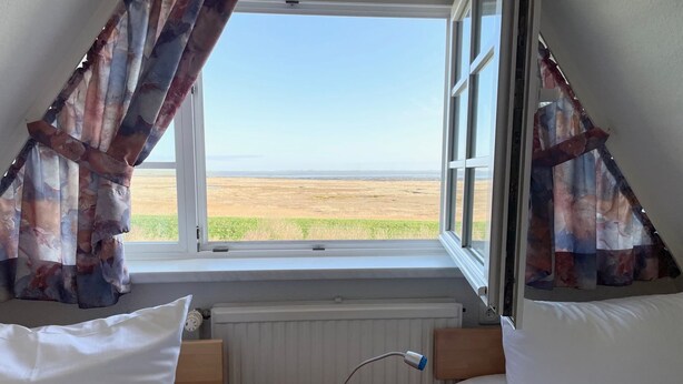 A bedroom with two beds, a window with curtains, a radiator, and a bedside table with a lamp. - Watt'n Blick, 70sqm for up to 4 people - Haus am Wattenmeer (Sylt)